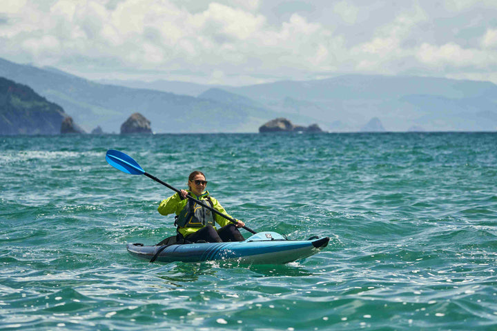 Paddling the Chelan 120 on the ocean, with rocky hills under a partly cloudy sky.