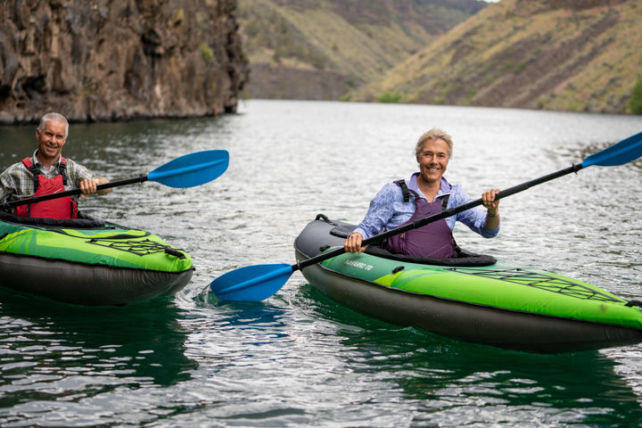 Two people paddle Navarro 110 kayaks on a calm, cliff-lined river.
