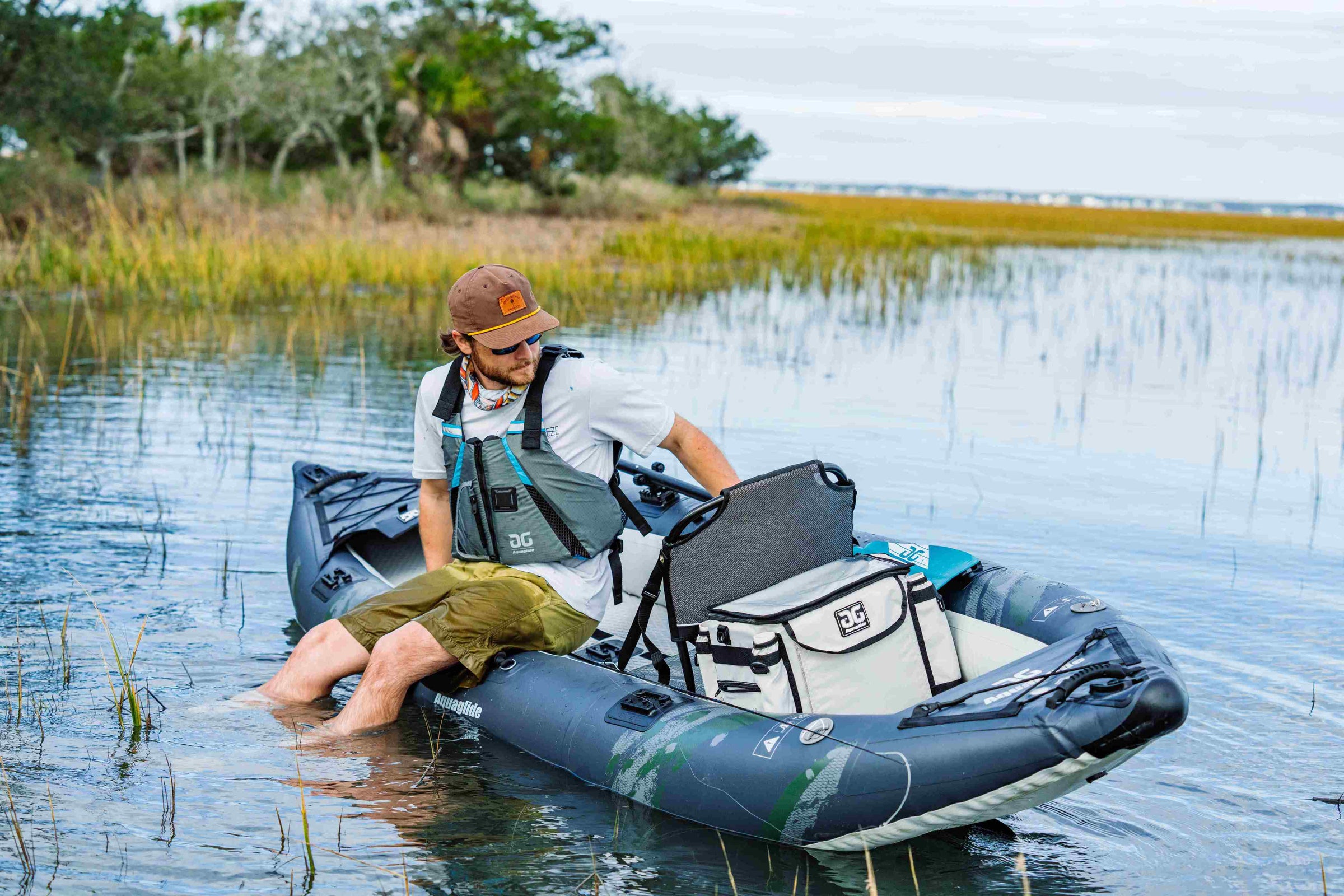 Person sitting on an inflatable kayak in shallow water with a cooler.