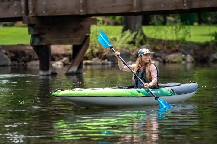A Navarro 110 paddler glides on a calm river under a wooden bridge.
