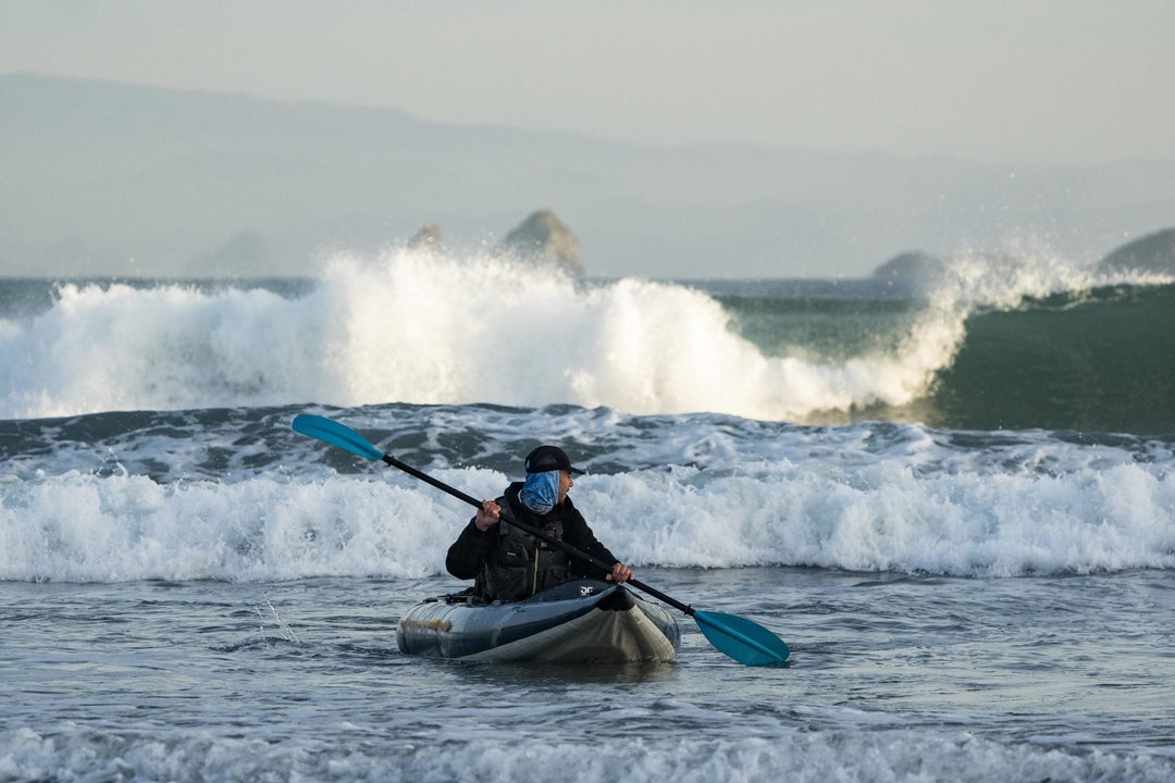Paddler in a kayak navigating the surf with waves splashing in the background.