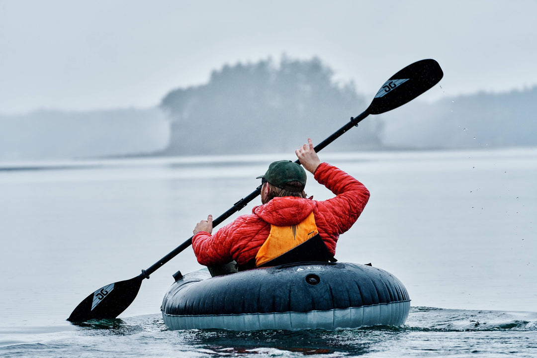 Man kayaking in a gray misty lake, wearing a red jacket.