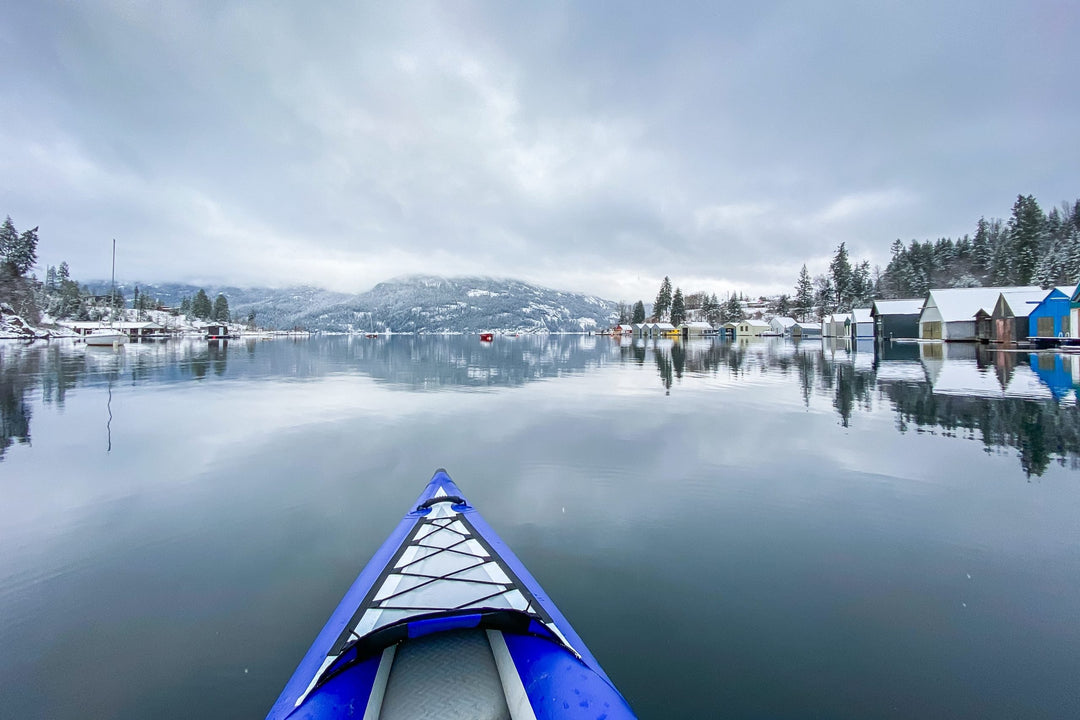 A kayak on a calm, snow-covered lake with mountains and houses reflected in the water.