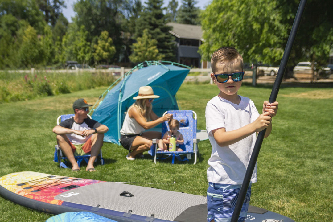 Boy holding paddle on a stand-up paddleboard with family in the background.