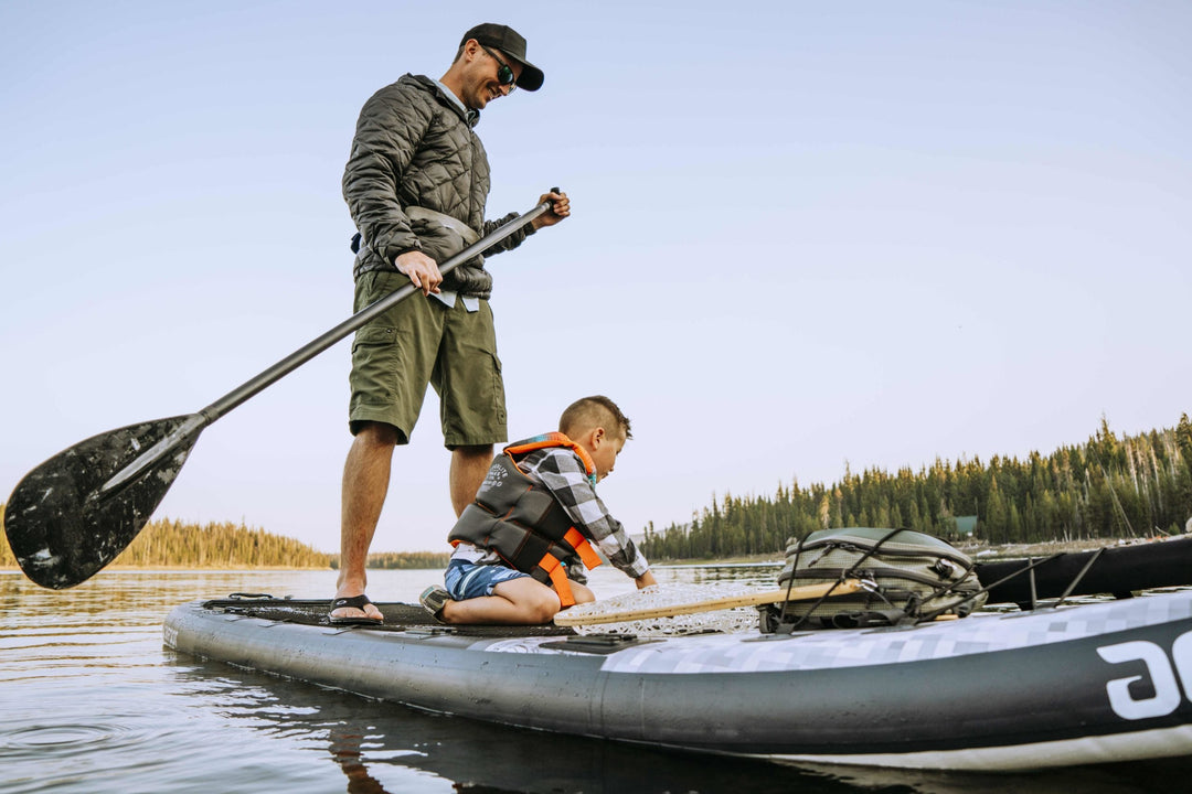 Man standing and paddling a paddleboard with a child kneeling on the board.