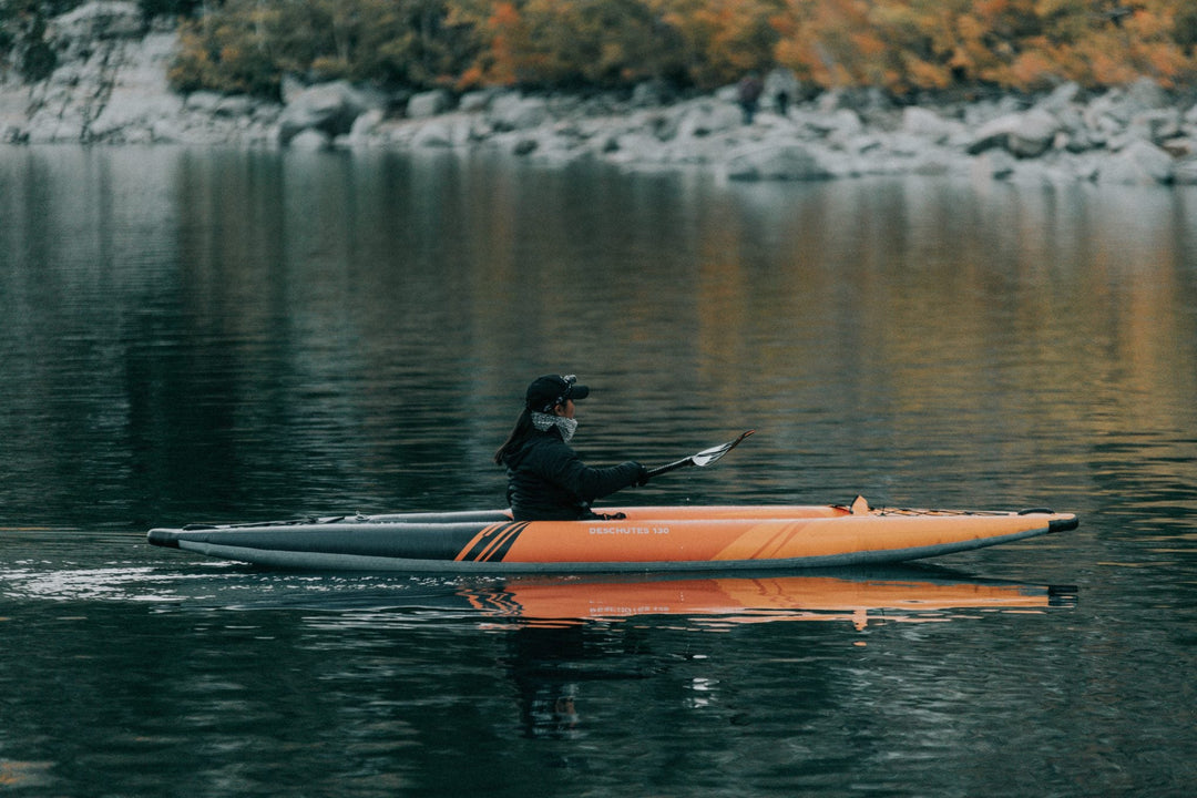 Person kayaking on a calm lake with fall foliage in the background.