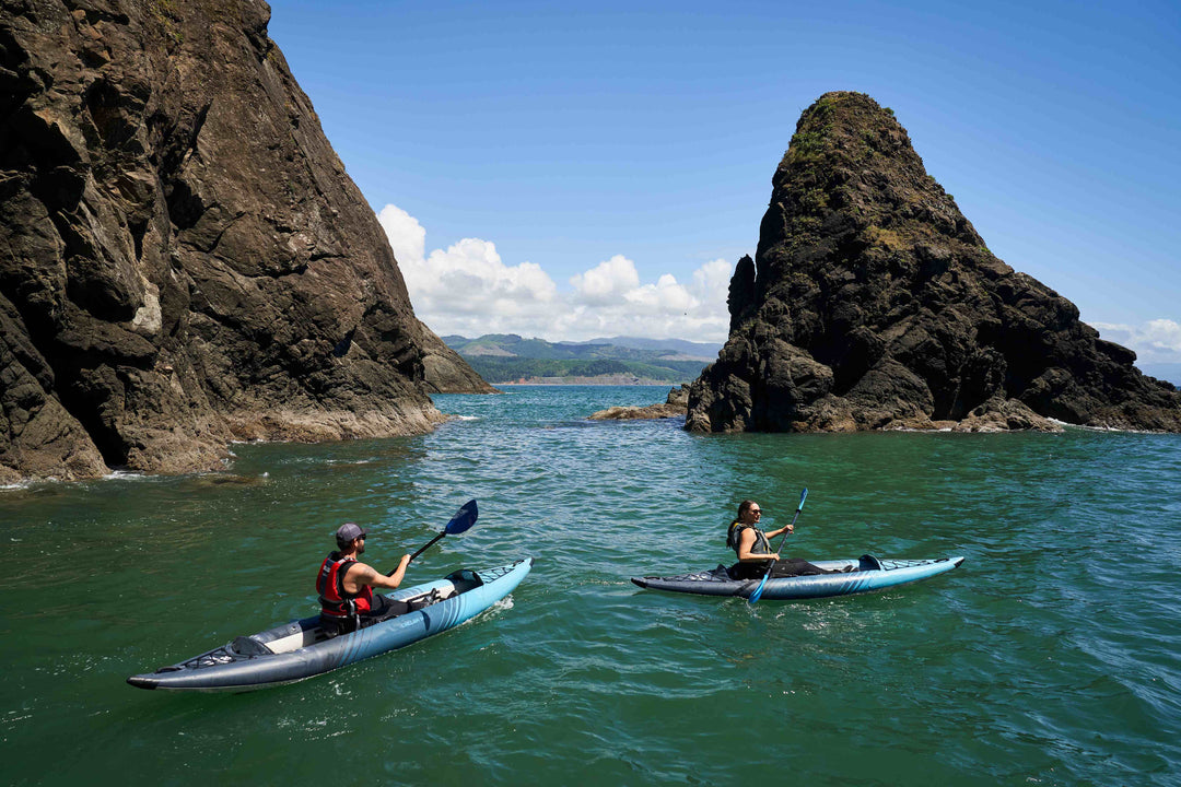 Man and woman kayaking near rocky cliffs on calm water.