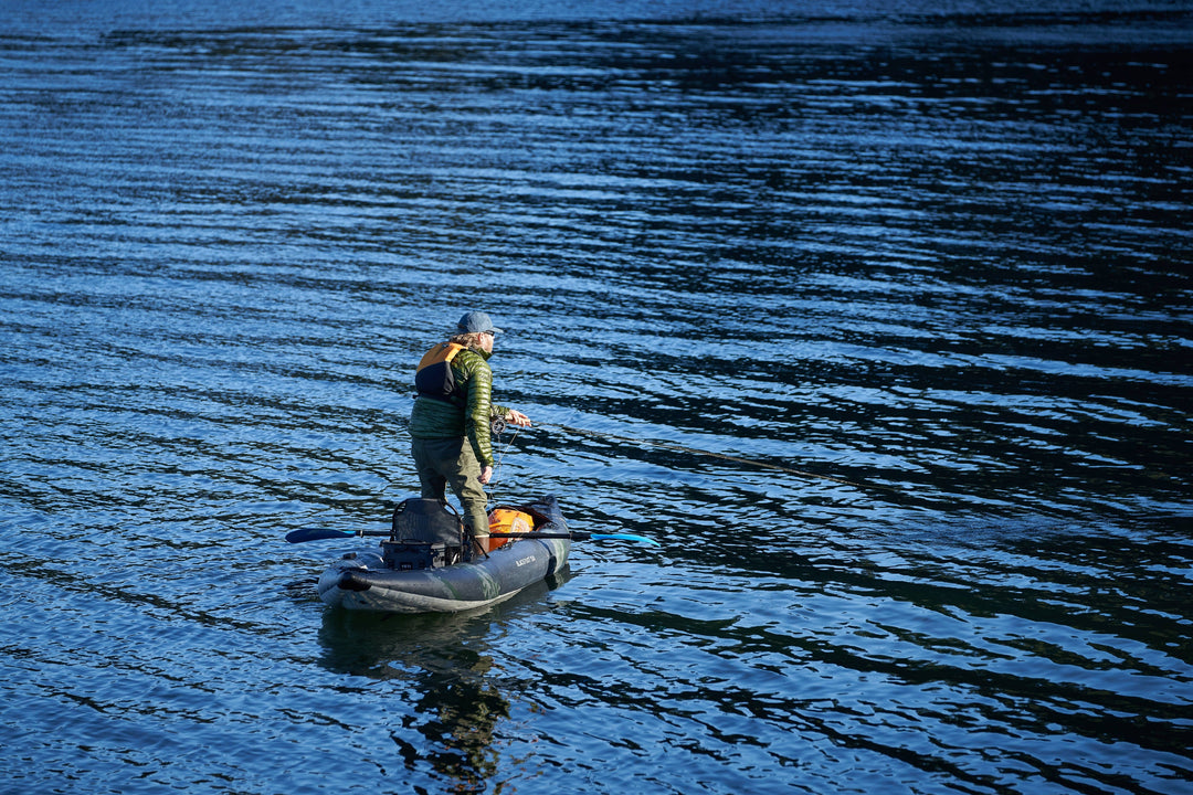 Man fishing while standing in a kayak on still water.