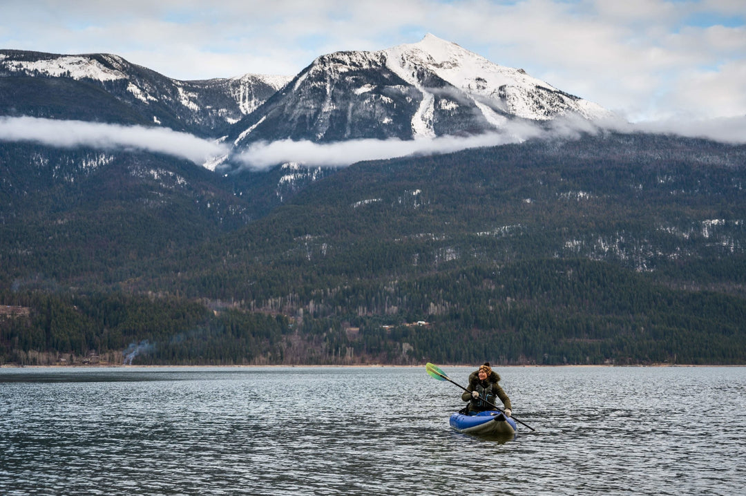 Person kayaks on a lake with snowcapped mountains in the background.