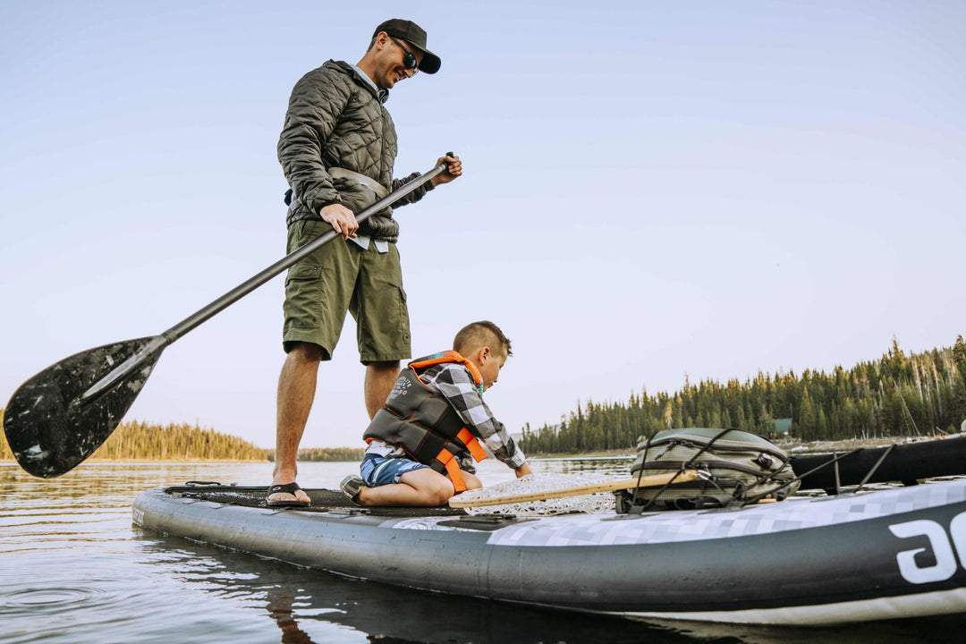 Man and child paddling on a board, man standing while child sits on the board.