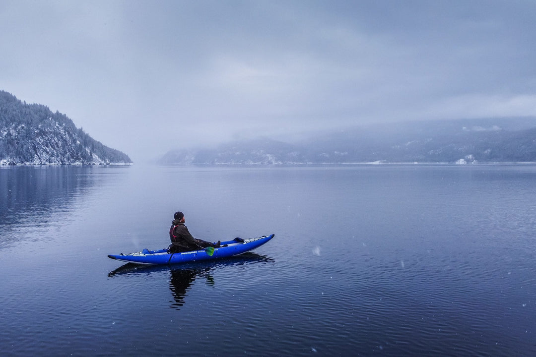 A person kayaking in a snowy landscape with a mountainous backdrop.