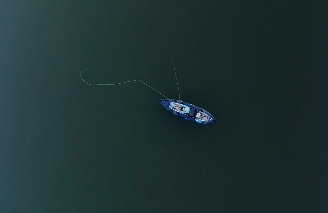 Aerial view of a lone person fishing from a small boat on calm, green water.