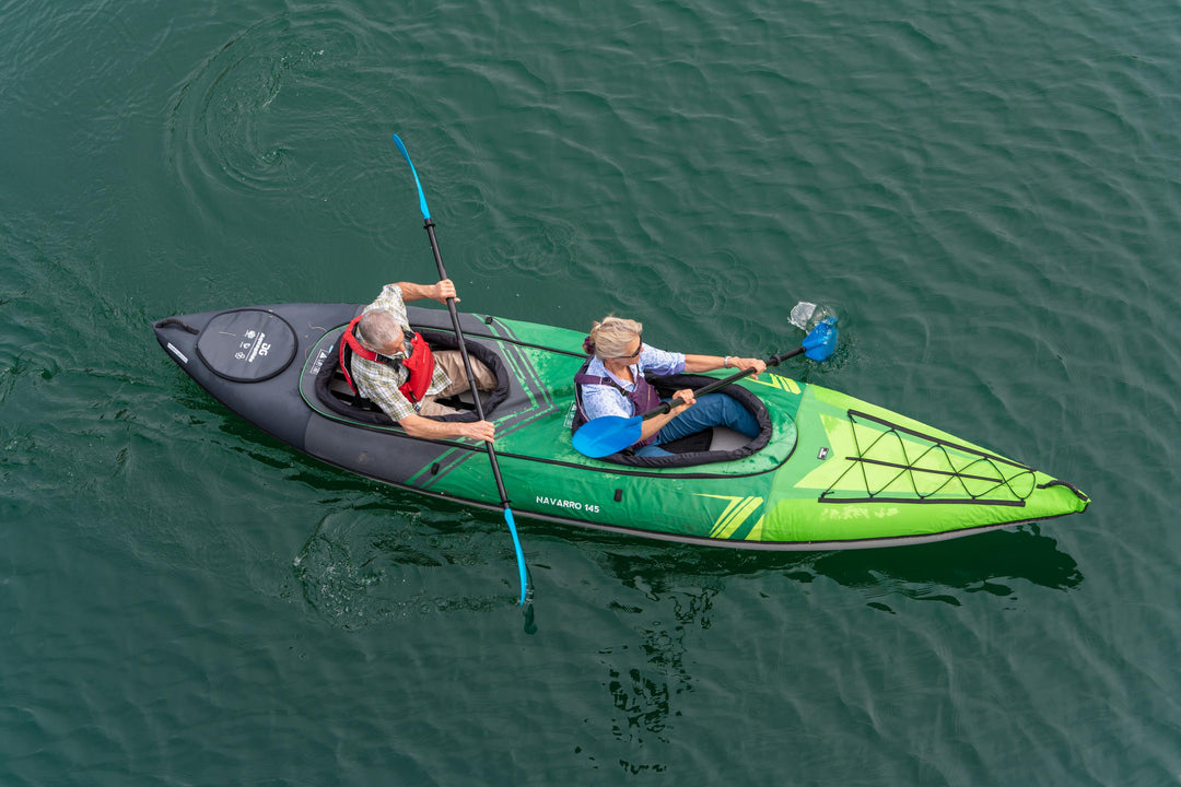 Two people kayaking in a green and black kayak on calm water, paddling in sync.
