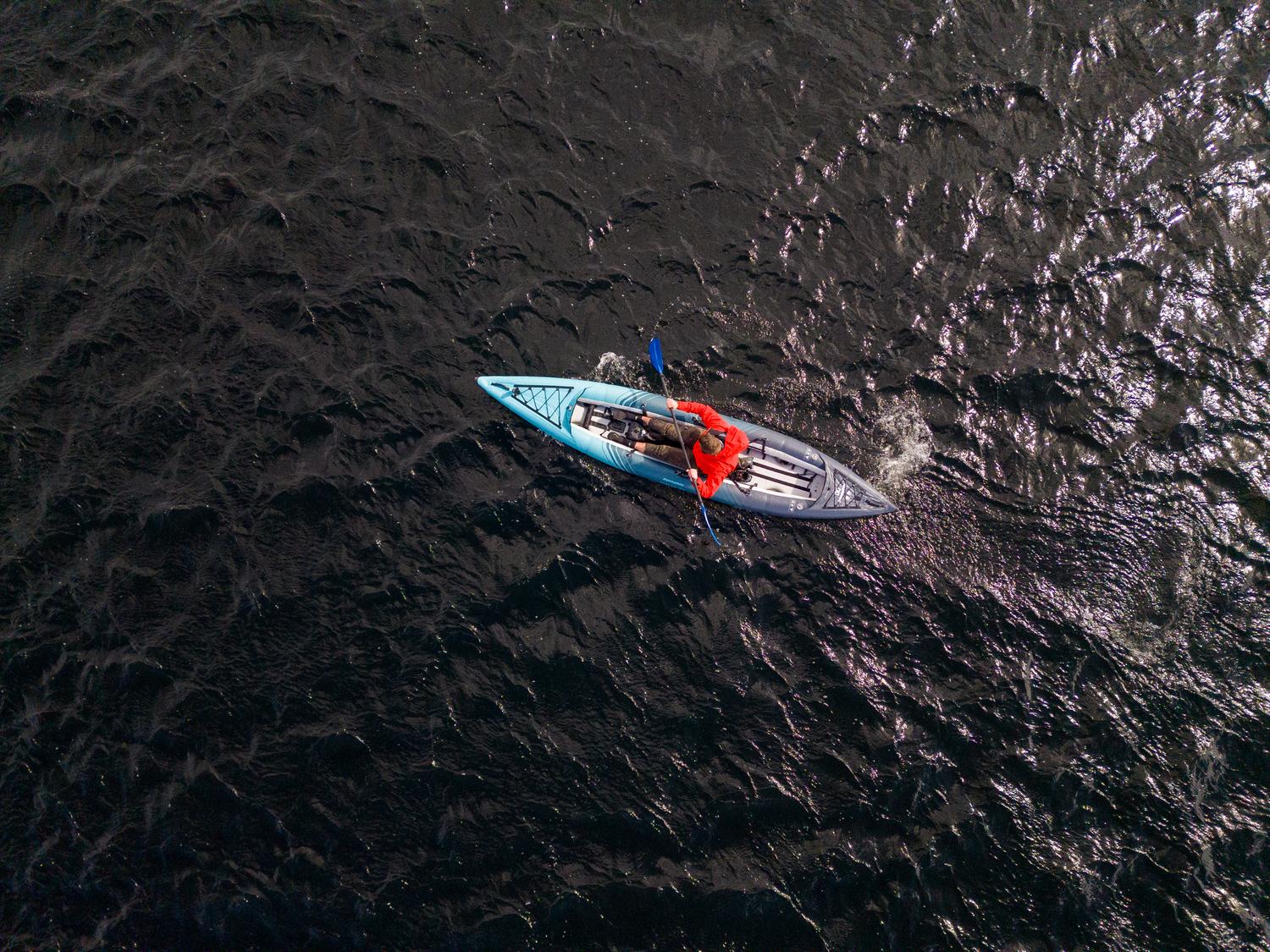 Person kayaking on dark wavy water, wearing a red jacket and using a blue paddle.