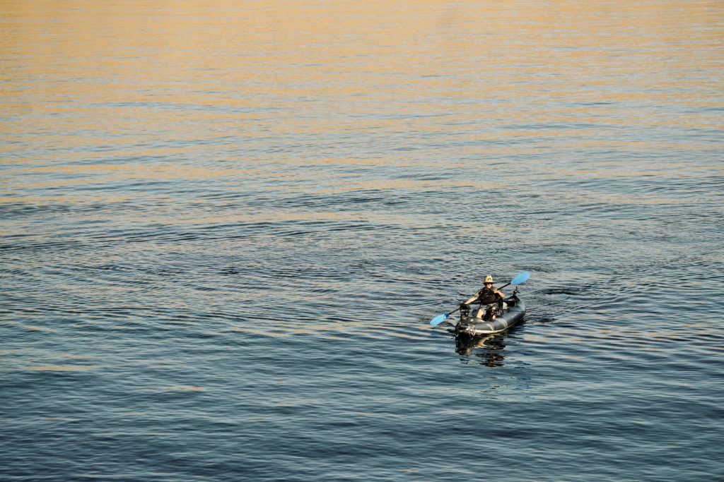Person kayaking on calm blue water with a tan reflection.