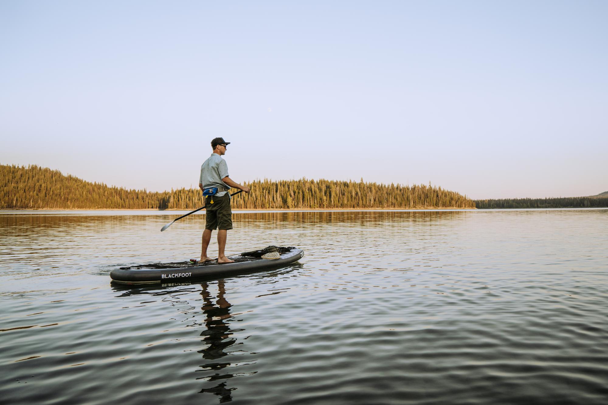 Person paddleboarding on a calm lake with a forested shore in the background.