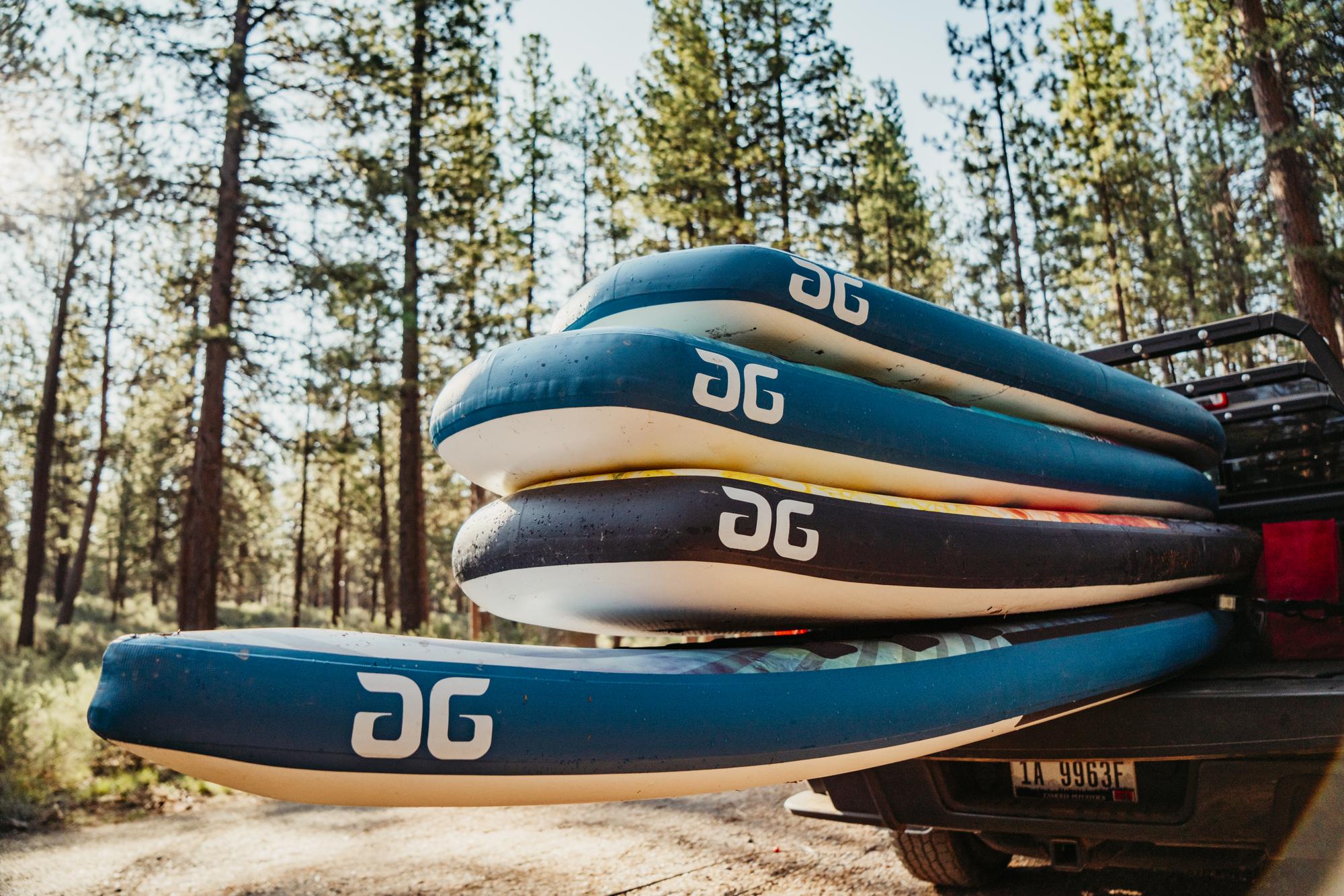 Four paddleboards stacked on a vehicle in a forested area.