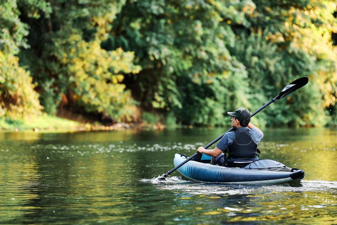 Paddler in a Chelan 120 glides through a calm river flanked by lush green trees.