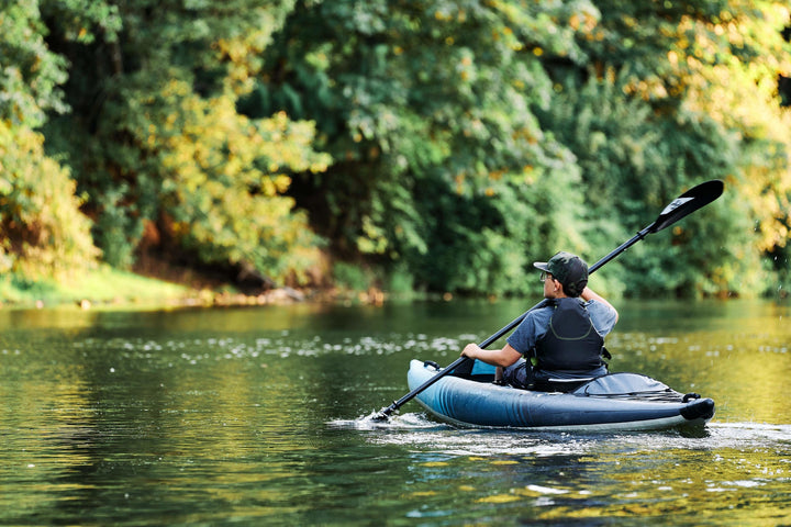 Paddler in a Chelan 120 glides through a calm river flanked by lush green trees.