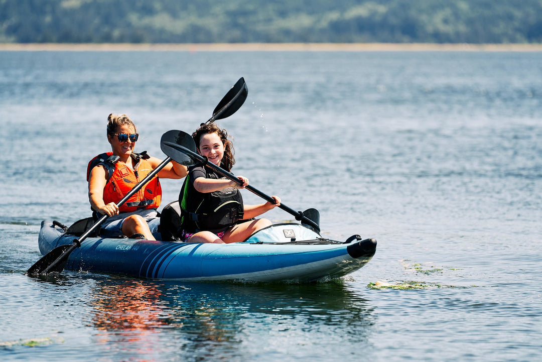 Two people in a Chelan 140 Package kayak on a calm lake under a clear sky.