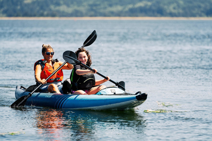 Two people in a Chelan 140 Package kayak on a calm lake under a clear sky.