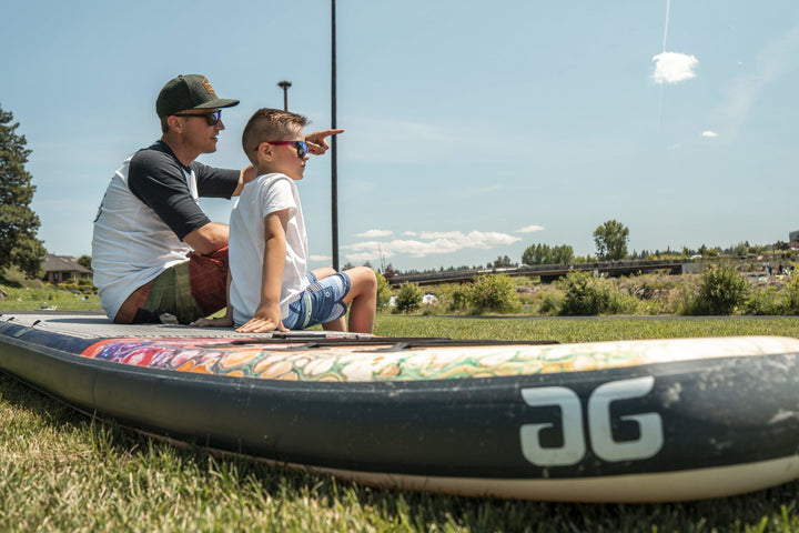 Two on the Kush 11 Paddleboard in a grassy area, one pointing forward.