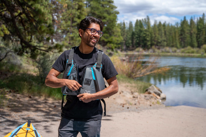 Person smiling by a lake in a black shirt and Aquaglide Paddle Vest, ready for kayaking.
