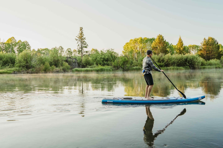 Paddling the Roam 126 Paddleboard on a calm lake, enjoying the lush trees and adventure.