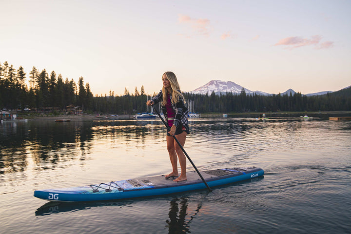 Paddleboarding at sunset on the Roam 126 Paddleboard, framed by mountains and trees.