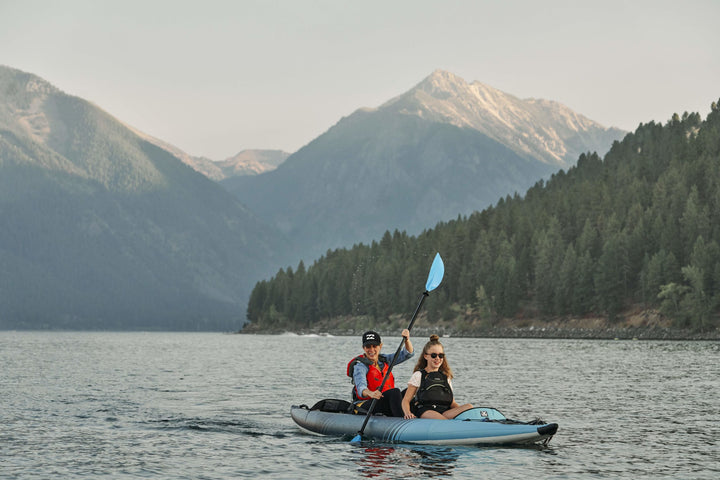 Two in a Chelan 155 kayak on a lake, surrounded by mountains and forests.