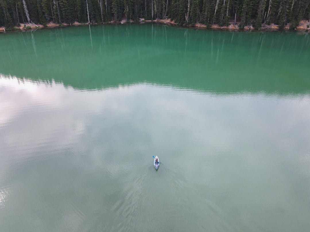 A person on the Cirrus Ultralight 110 glides across a calm, green lake surrounded by forest.