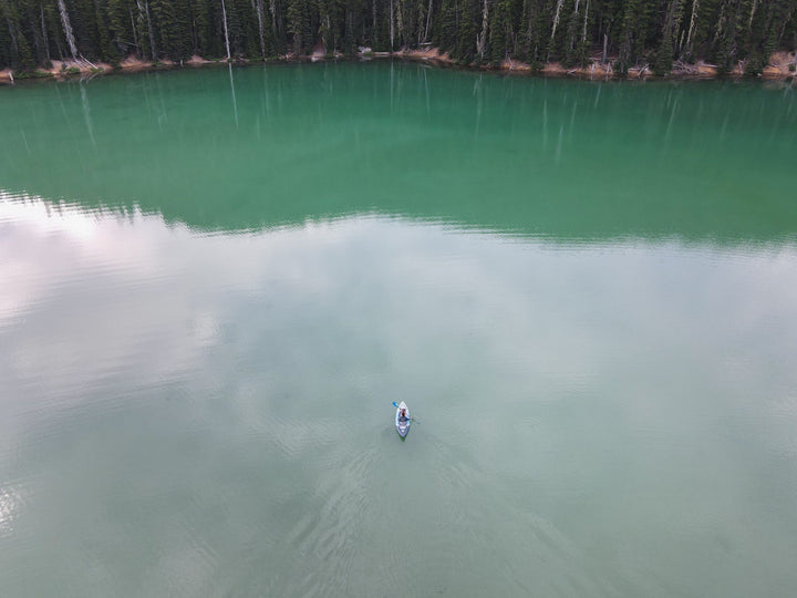 A person on the Cirrus Ultralight 110 glides across a calm, green lake surrounded by forest.