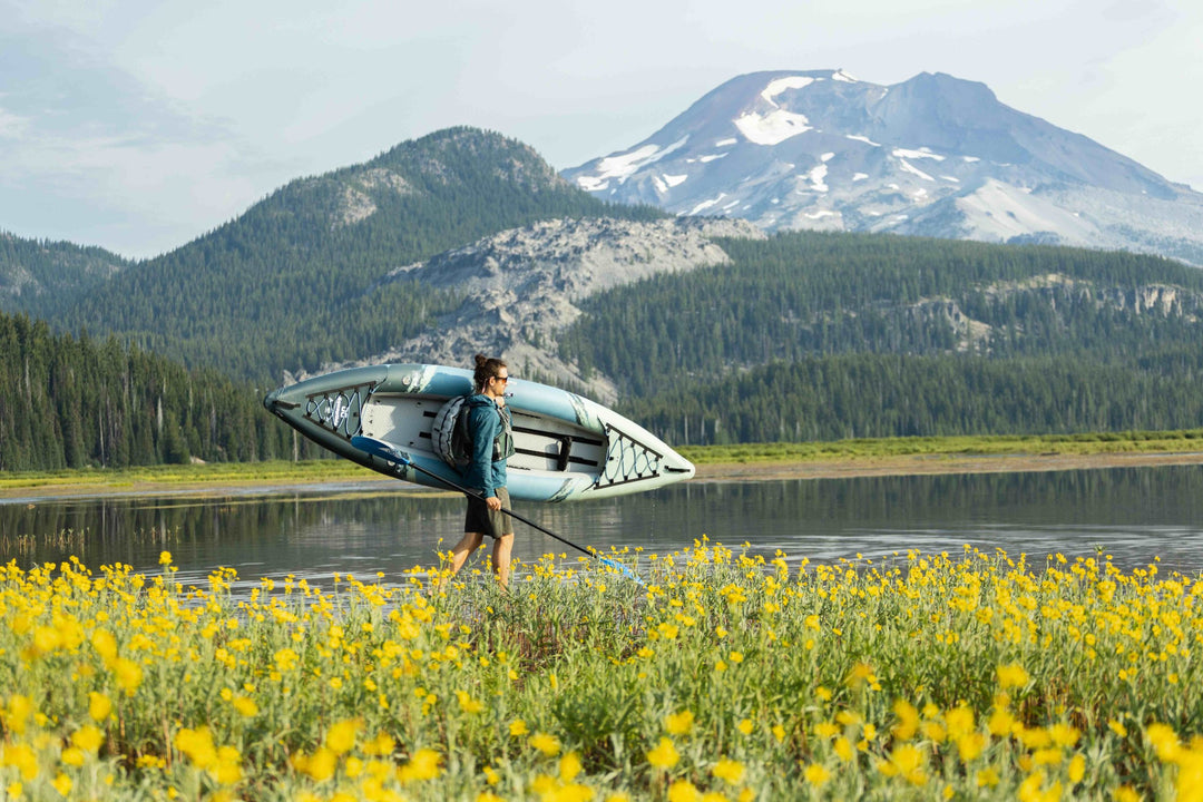 Beside a lake with mountains and yellow wildflowers, carrying the Cirrus Ultralight 110 kayak.