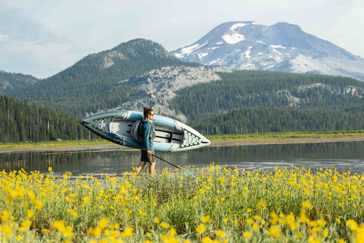 Beside a lake with mountains and yellow wildflowers, carrying the Cirrus Ultralight 110 kayak.