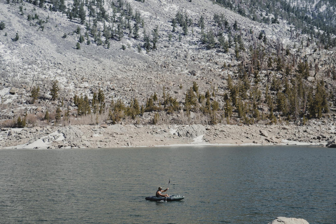 Backwoods Expedition 85 kayak gliding on a calm lake, surrounded by rocks and pine trees.