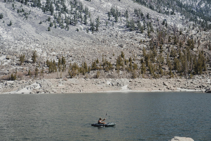 Backwoods Expedition 85 kayak gliding on a calm lake, surrounded by rocks and pine trees.