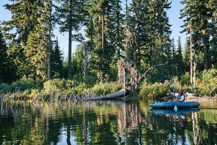Paddler fishing from a Backwoods Expedition 85 kayak on a forested lake.