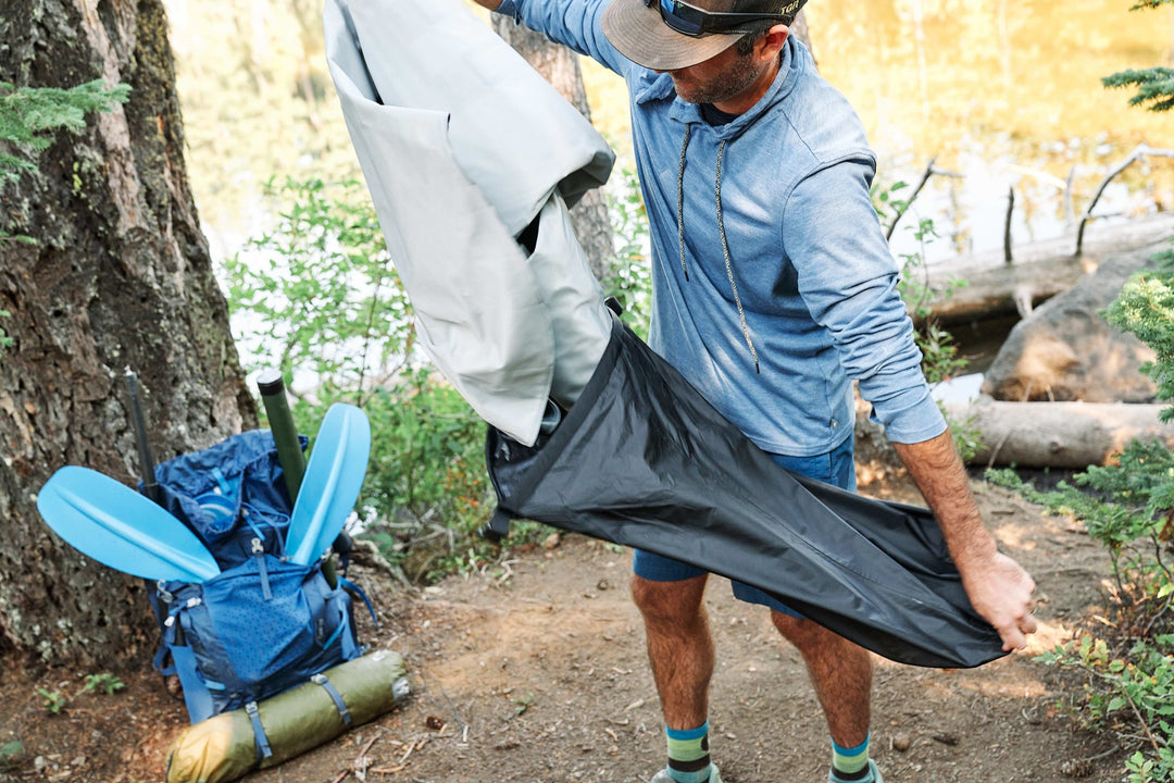 Man sets up tent with a Backwoods Angler 75 backpack and oars for solo kayak adventures.