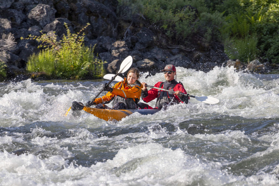 Two paddle the McKenzie 125 through whitewater rapids, surrounded by lush greenery.