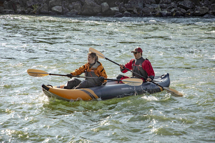 Two people tandem paddling a river in the McKenzie 125, wearing life jackets.