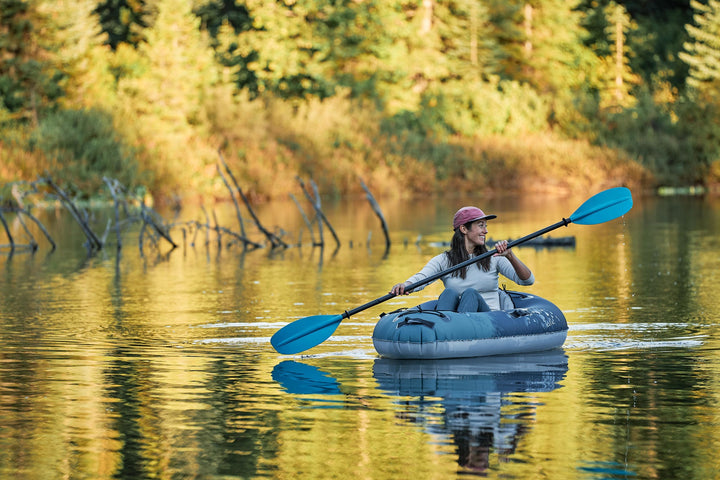 Solo paddling Backwoods Purist 65 on a calm lake, surrounded by trees under a clear sky.